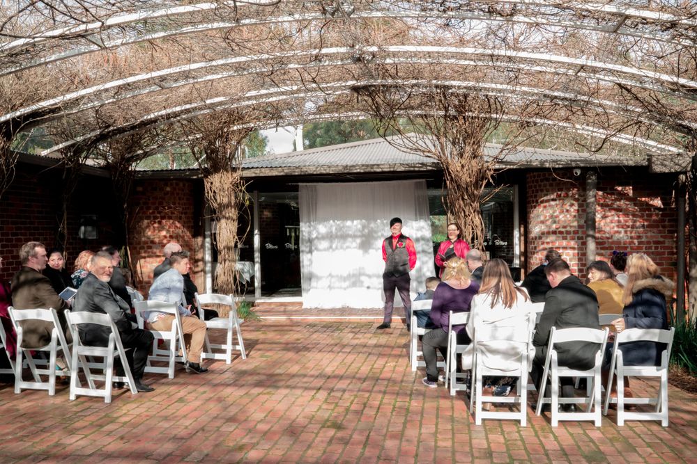 Outdoor wedding ceremony setup with brick walls and white chairs under covered courtyard.