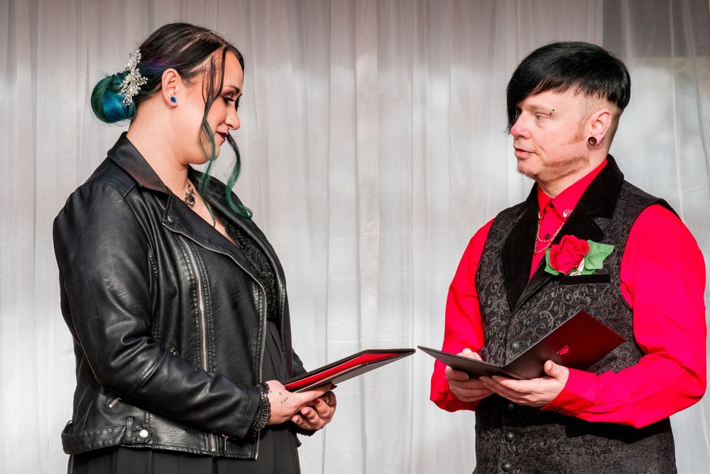 Bride in black dress and groom in black vest in  exchange documents during  a wedding ceremony.