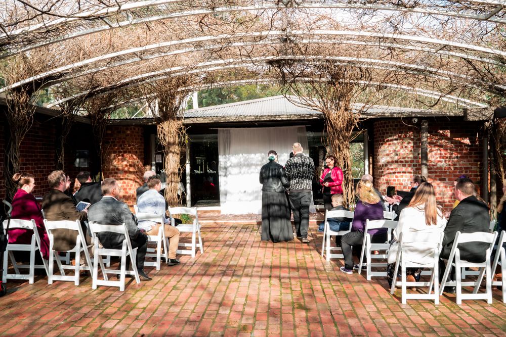 Wedding ceremony in progress at rustic brick venue with white folding chairs.