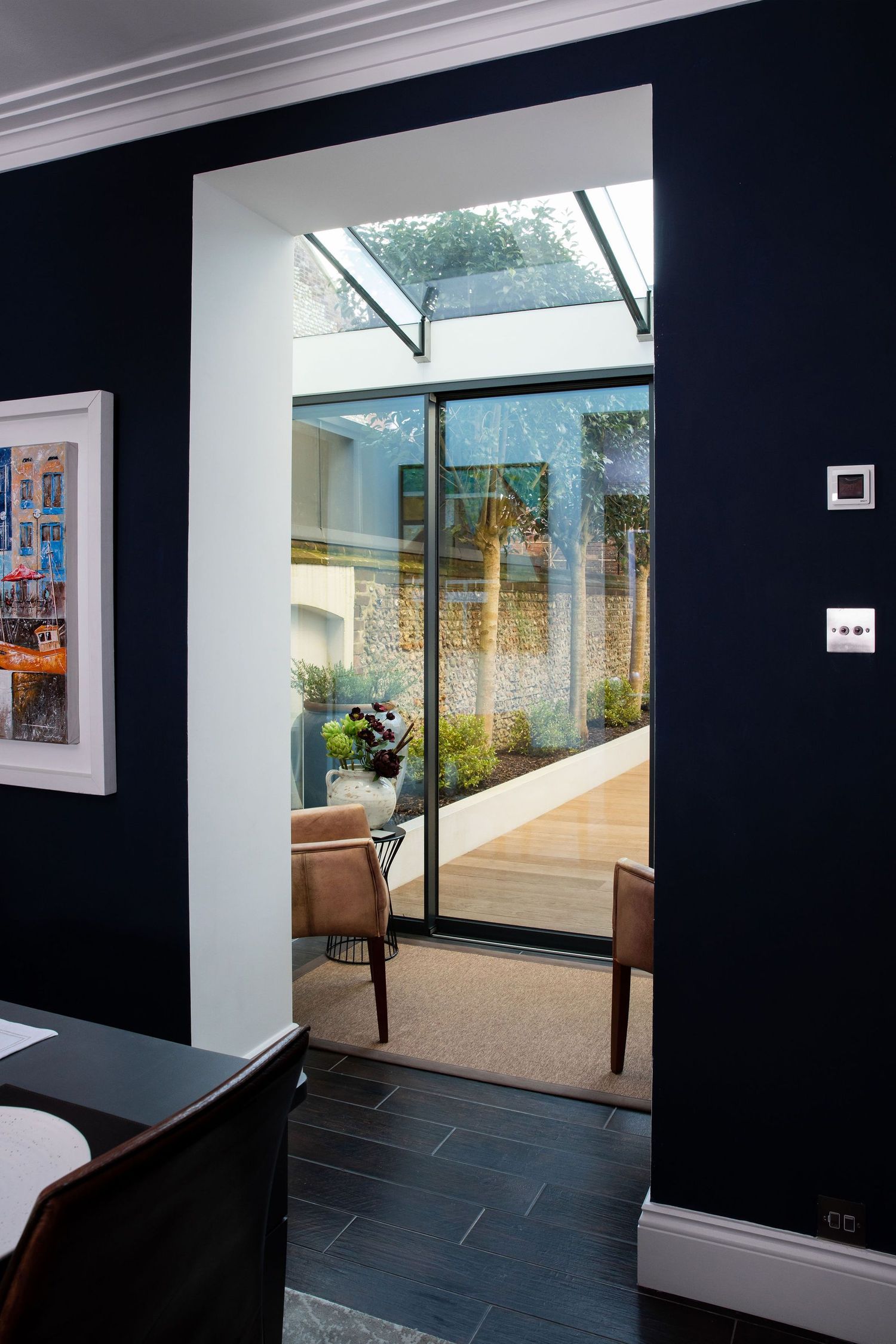 Modern glass extension with skylight leads to a bright garden room with dark navy walls.
