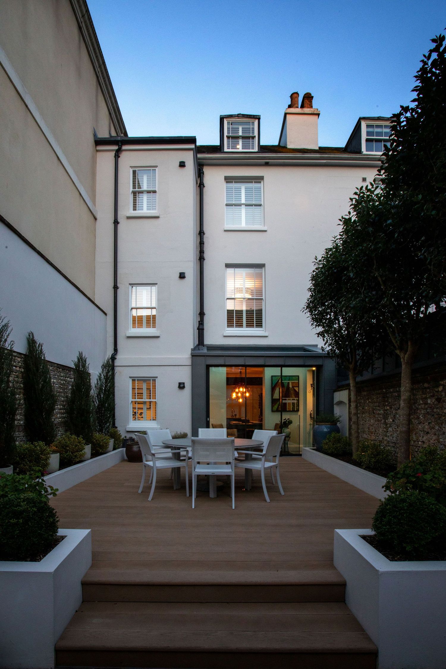 Elegant townhouse backyard features composite decking and outdoor dining area illuminated at dusk.