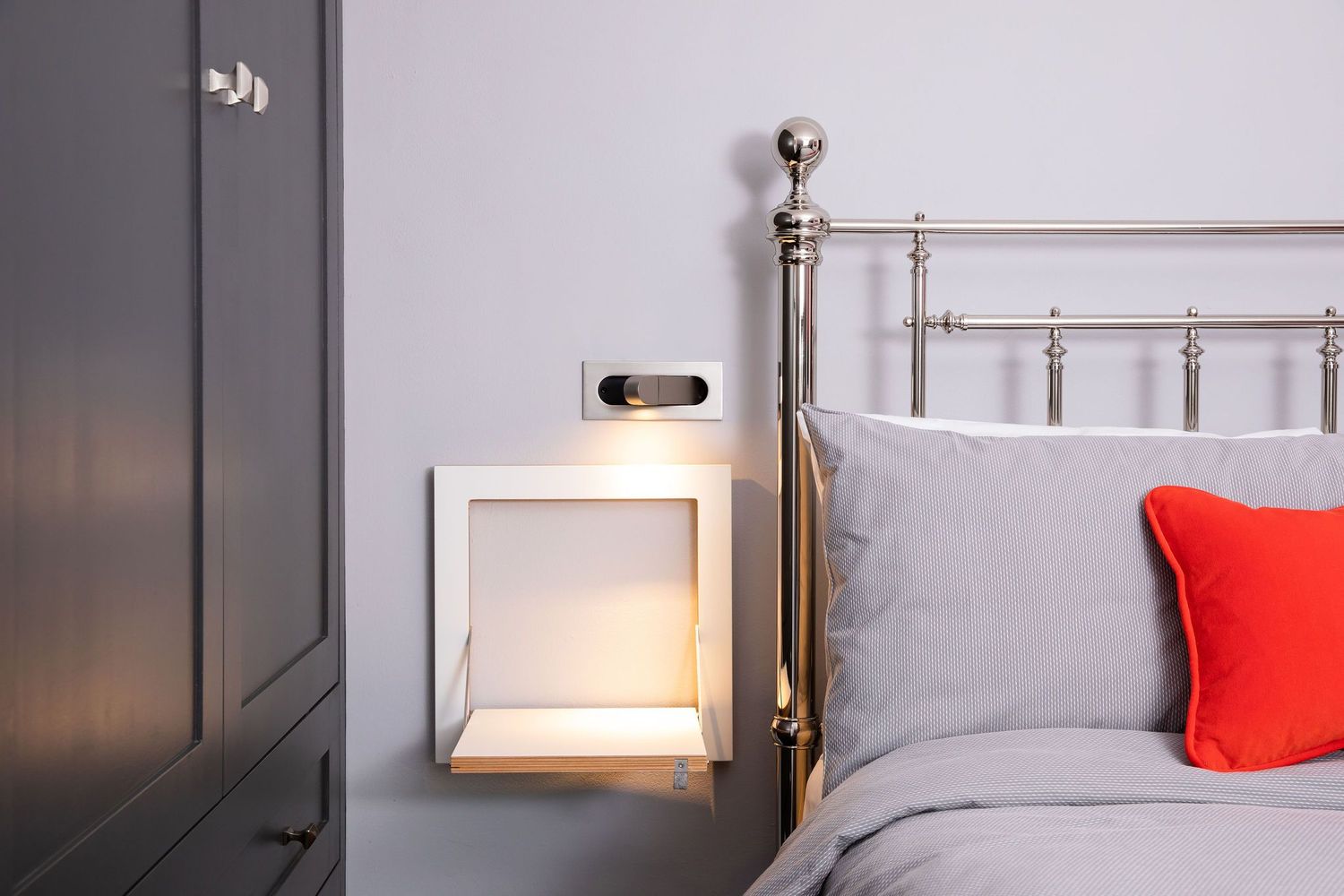 Minimalist bedside wall sconce next to metal headboard with gray and red pillows.