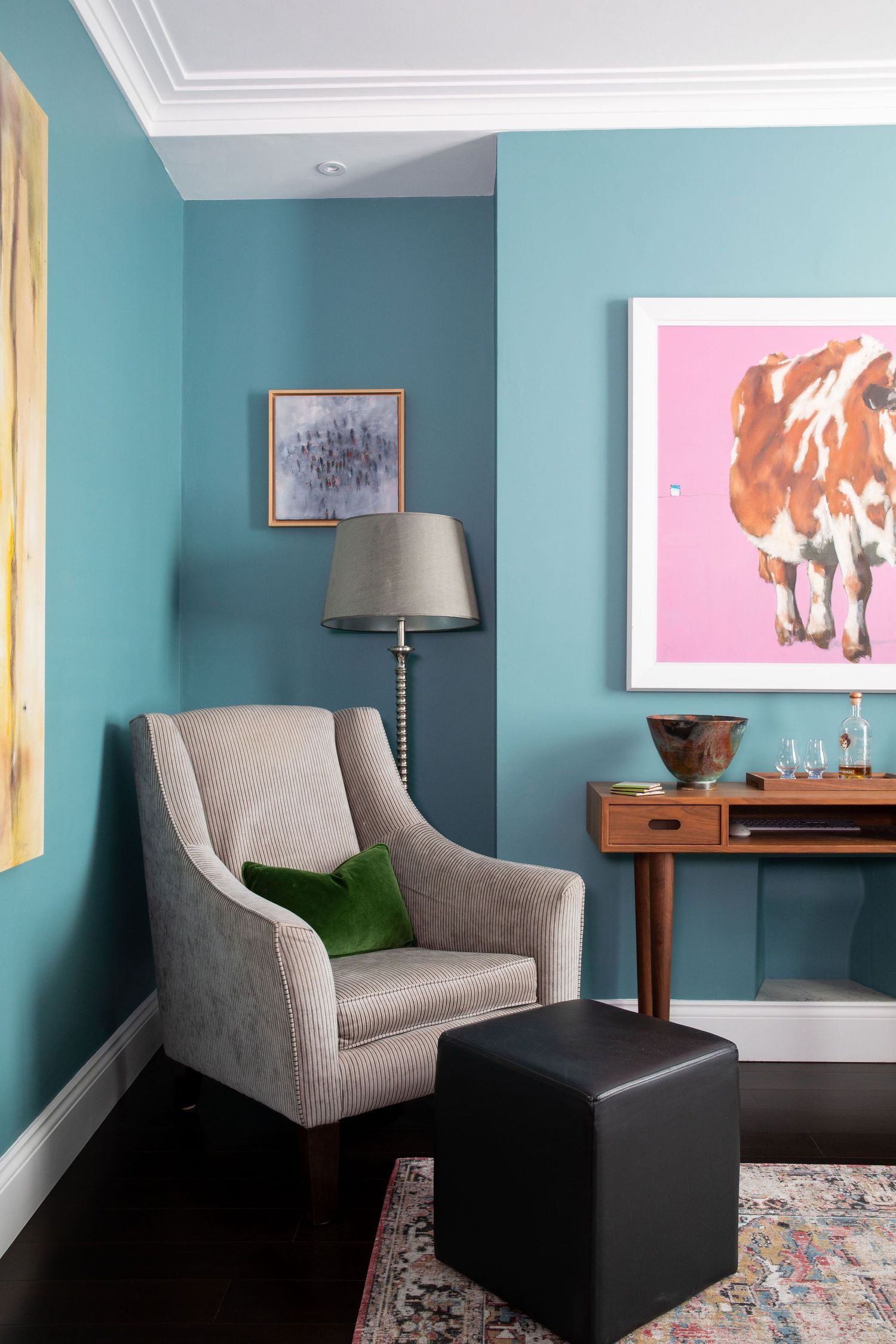 Cozy reading nook with gray armchair and cow artwork against turquoise walls.