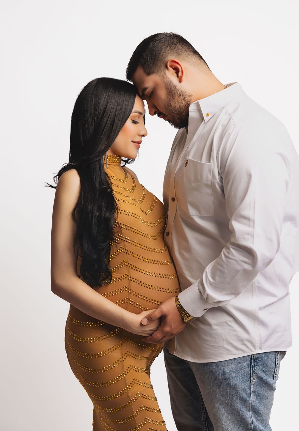 A tender maternity moment between a couple against a white background.