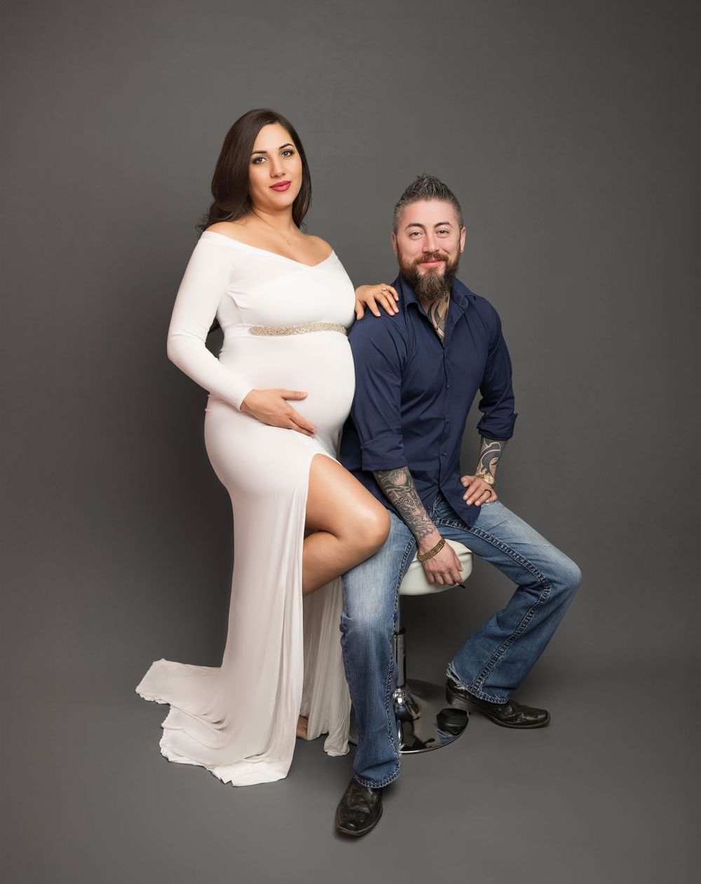 Studio maternity photo featuring couple in contrasting white dress and navy casual wear.