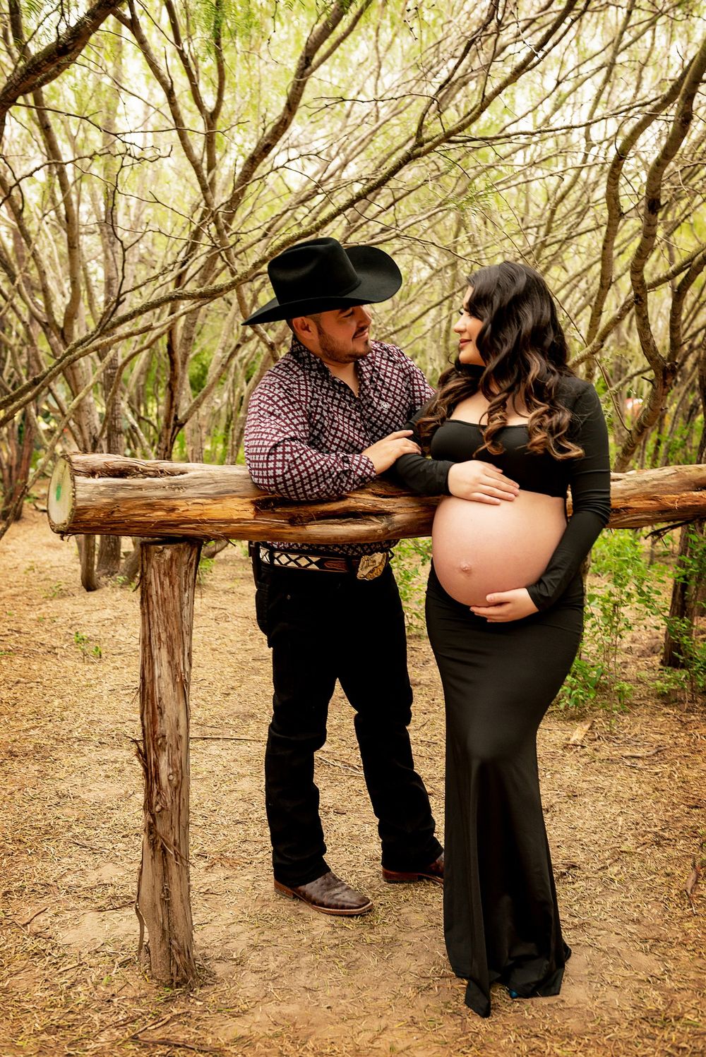 Rustic maternity photo shoot in wooded setting with couple by wooden fence.
