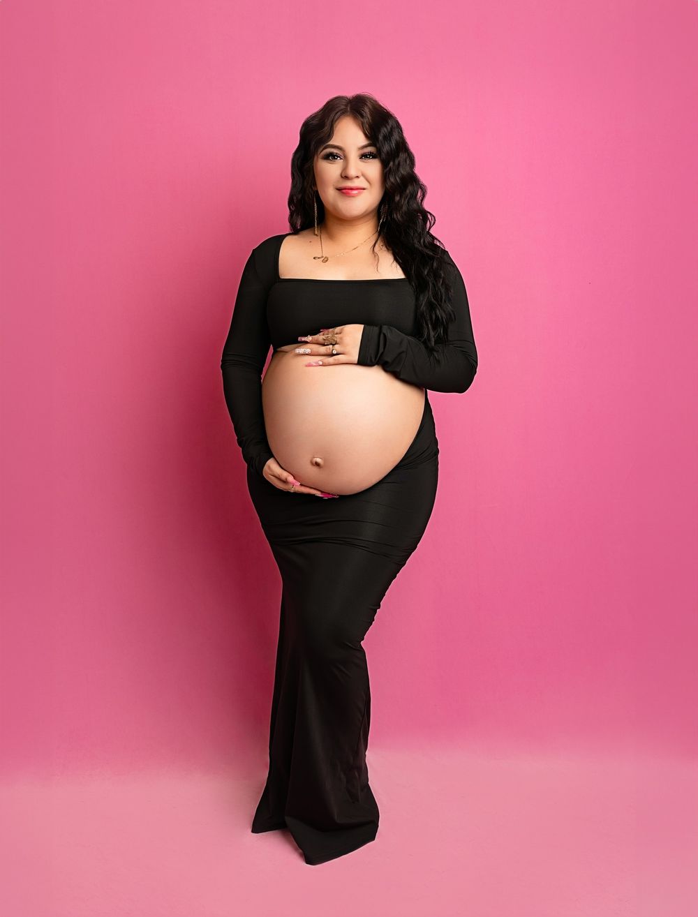 Maternity photo against pink background with woman in black dress.