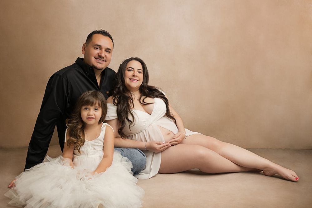 Studio portrait of family in white outfits against beige background.