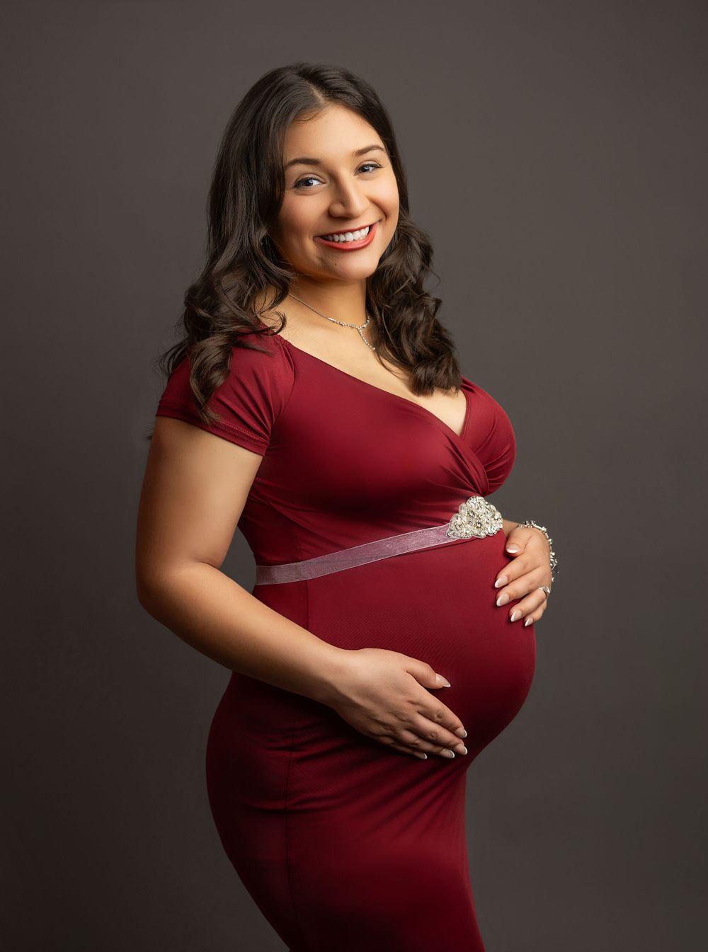 Portrait of an expectant mother in a burgundy dress against dark background.