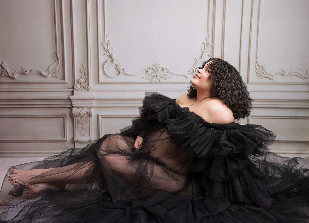 Dramatic portrait in a black tulle gown against ornate white wall panels.
