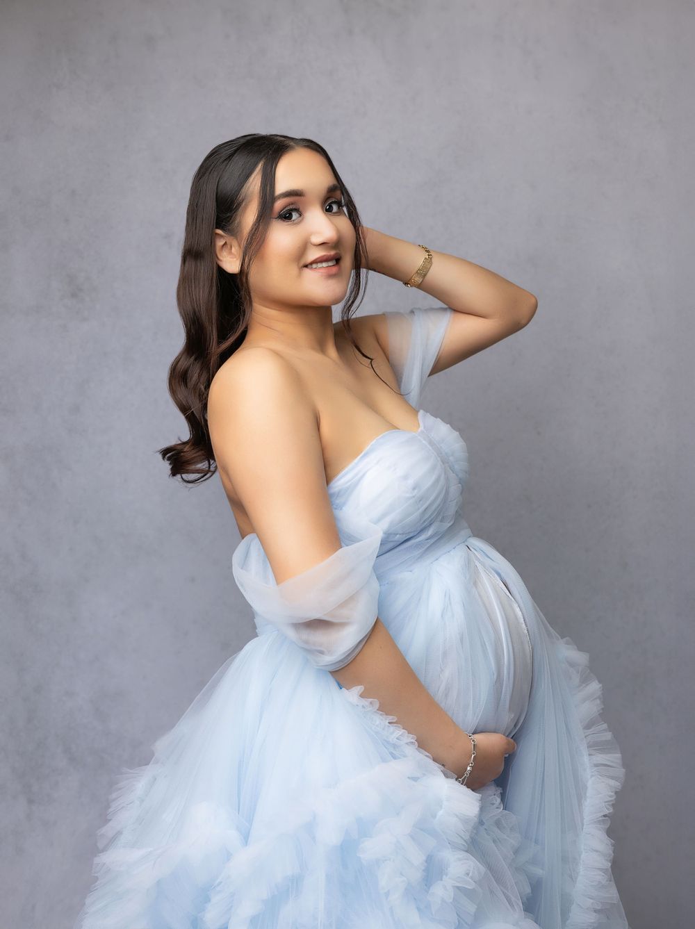 An ethereal maternity portrait showcasing a flowing light blue tulle gown in a studio setting.