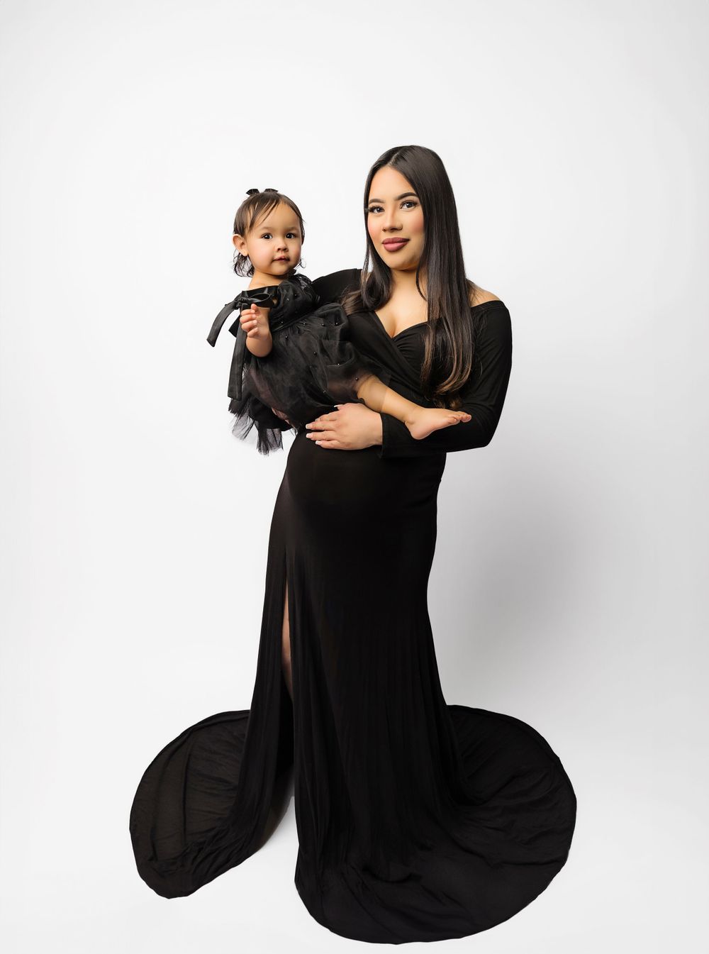 Studio portrait of parent and child in matching black formal attire against white background.