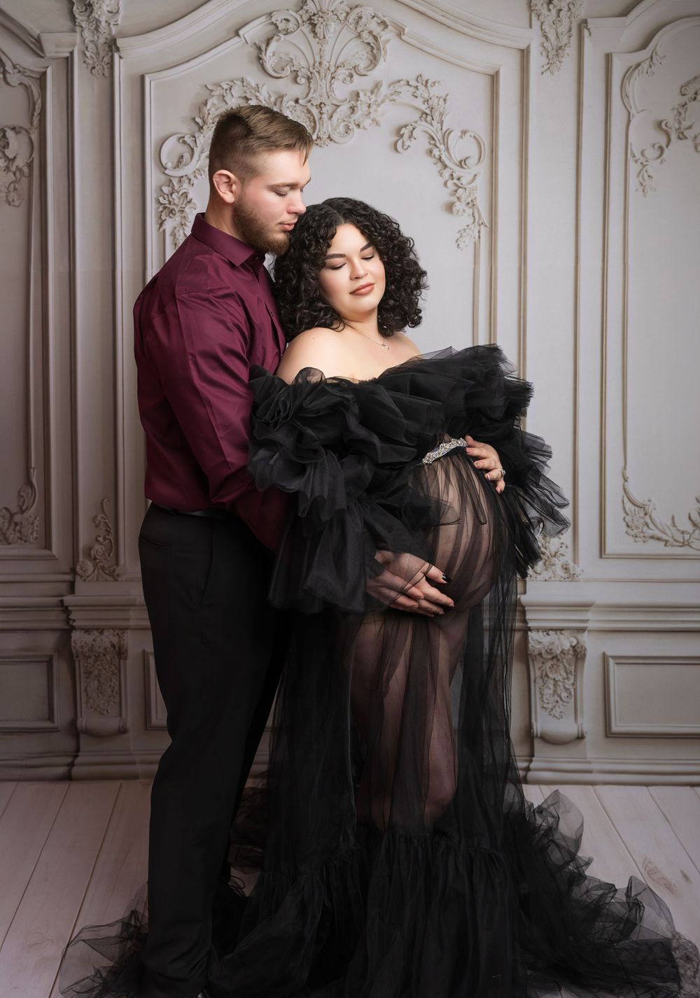 Intimate maternity portrait with a black tulle gown against classic white wall panels.