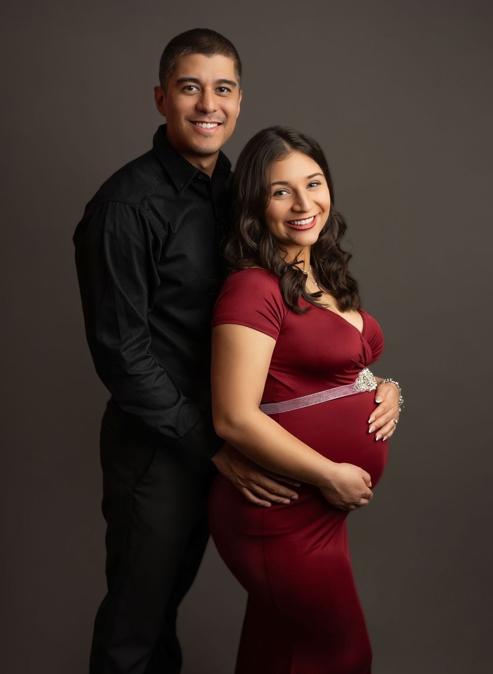 Elegant maternity portrait of couple in formal attire against dark background.