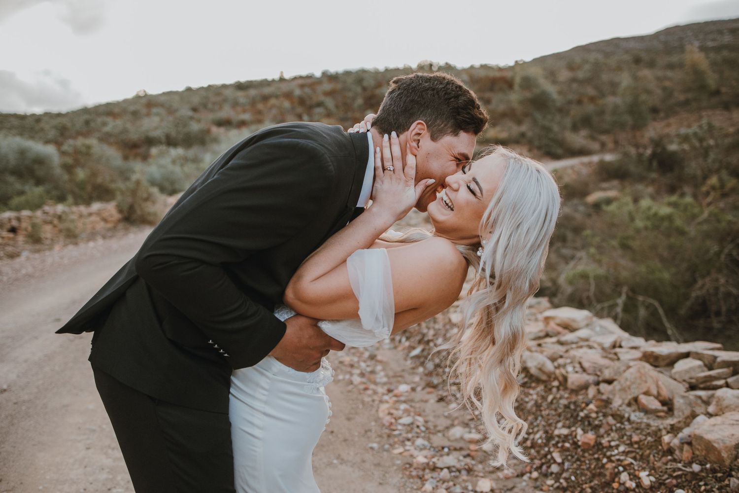 Romantic couple in wedding attire sharing a tender moment on a mountain path.