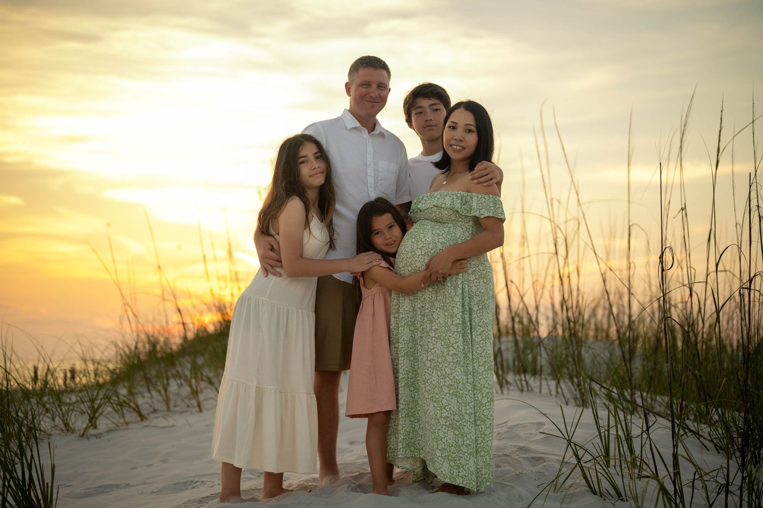 A group stands together watching sunset on a beach with sea oats in foreground.