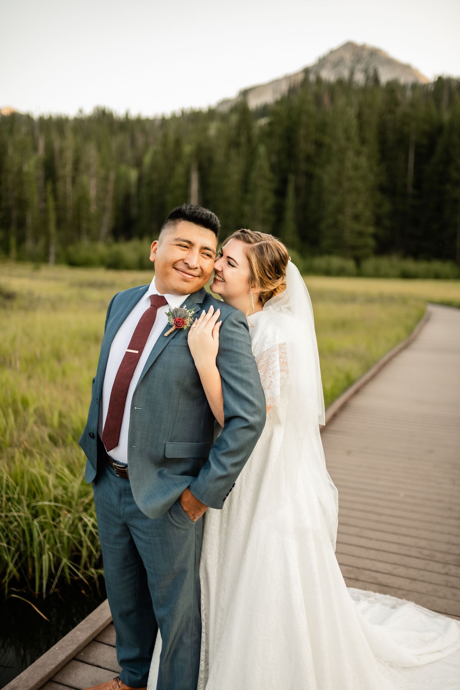 Wedding couple sharing joyful moments on a wooden boardwalk with mountain scenery.