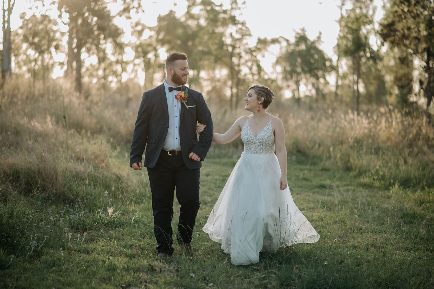 Couple walking together through tall grass in wedding attire.