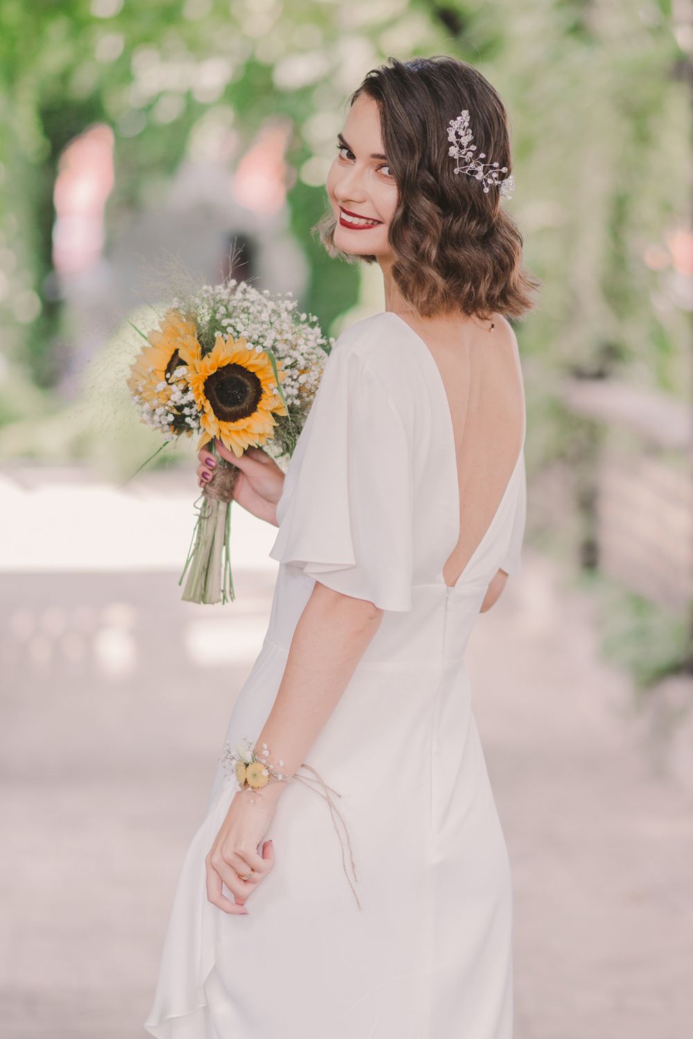 A white wedding dress with flutter sleeves and a sunflower bouquet in a garden setting.