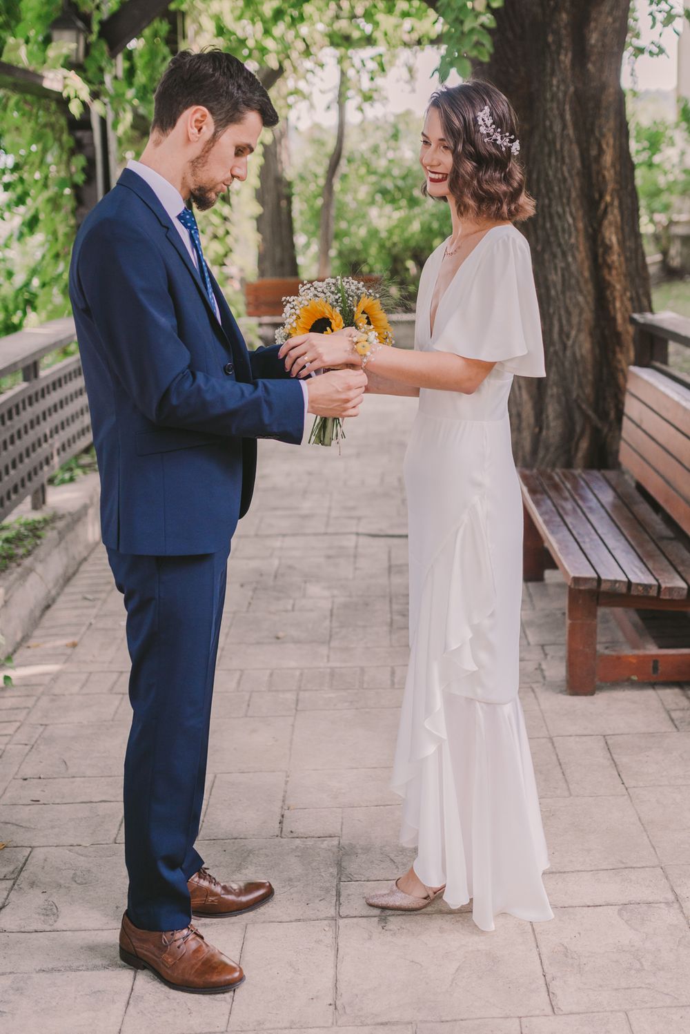 Bride and groom share first look moment on stone pathway with sunflower bouquet.