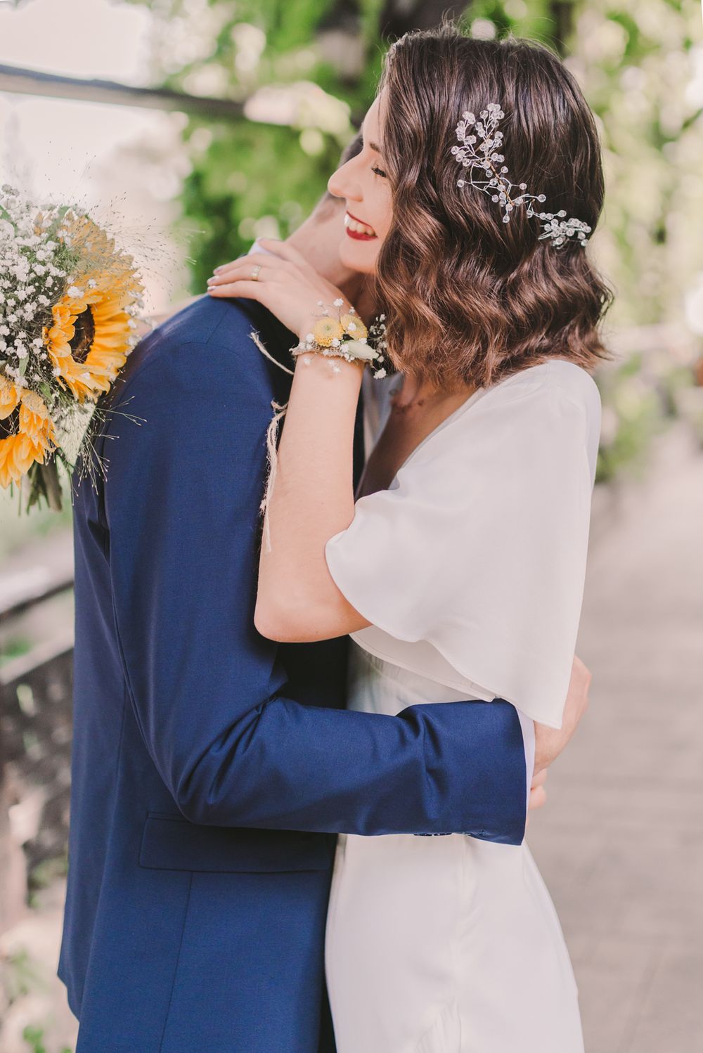Wedding couple embracing with sunflowers and white florals in outdoor garden setting.