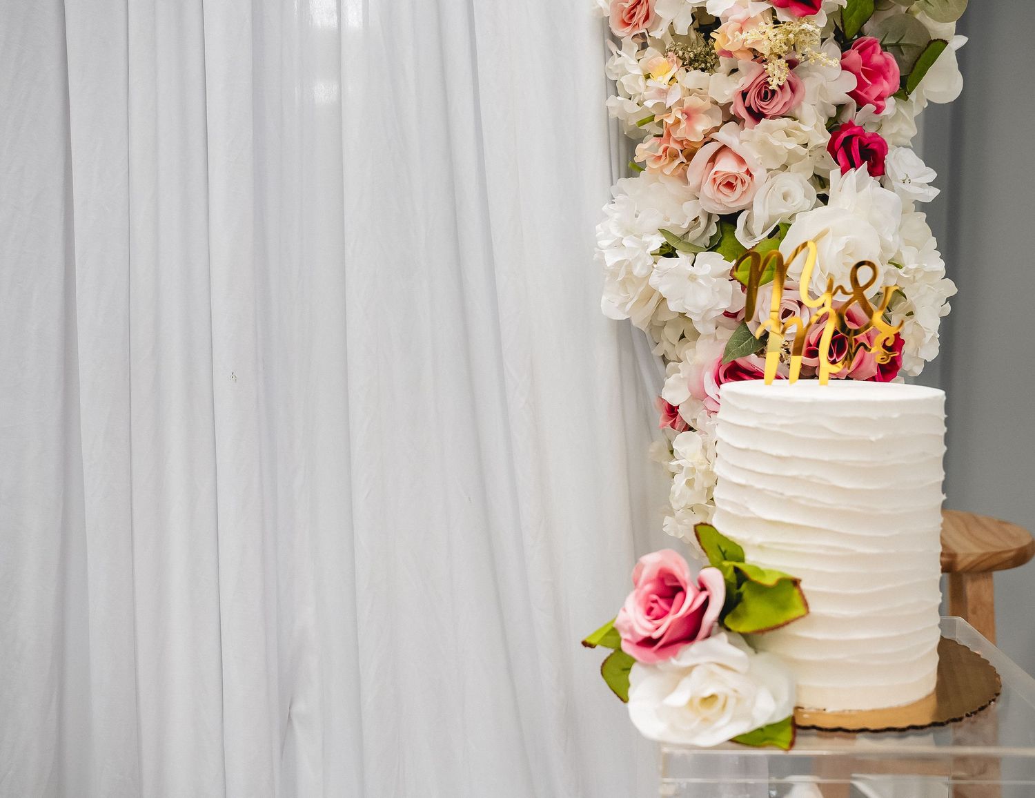 Elegant white wedding cake decorated with pink and peach flowers against a white backdrop.