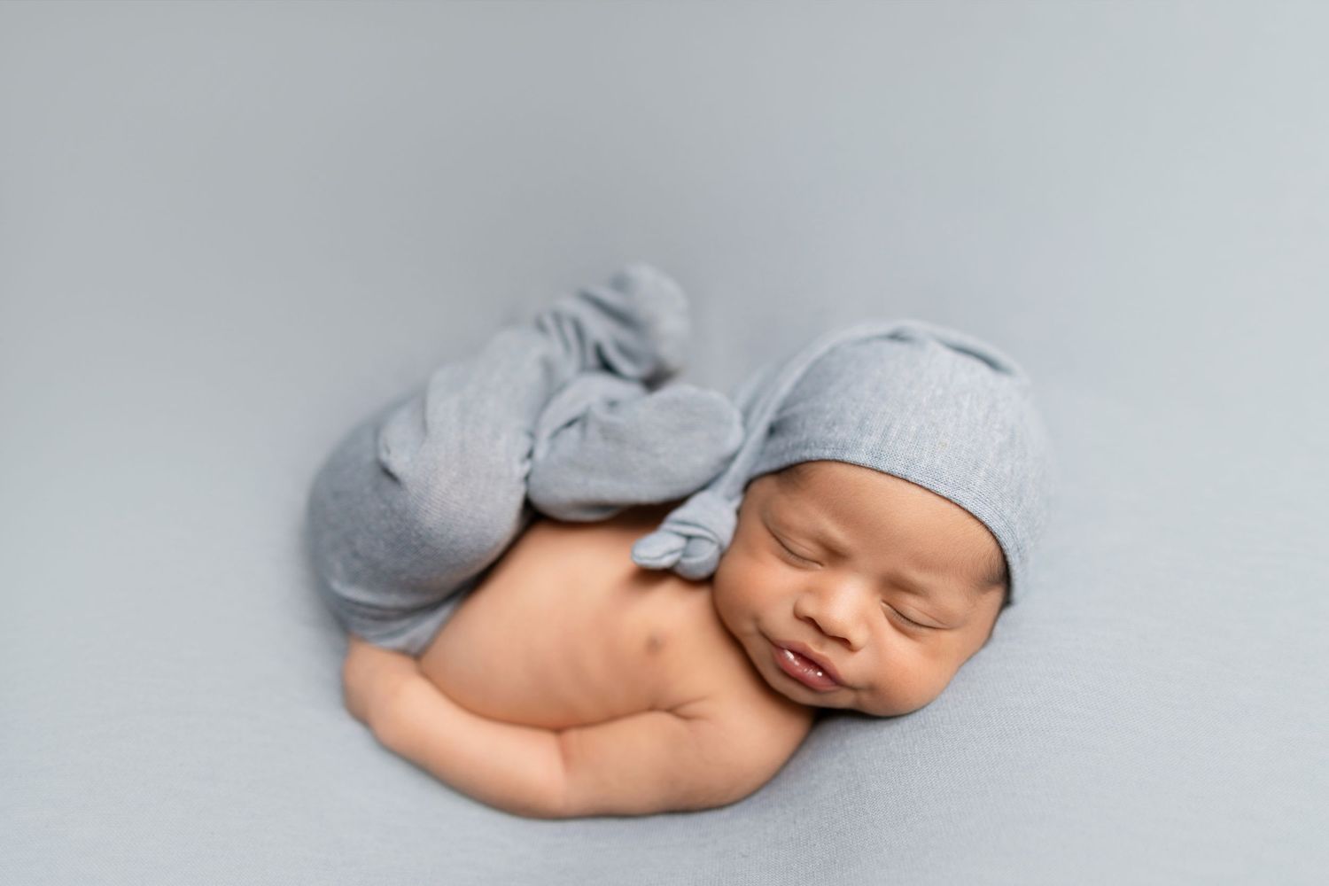 Sleeping newborn wearing soft gray hat during minimalist portrait session.
