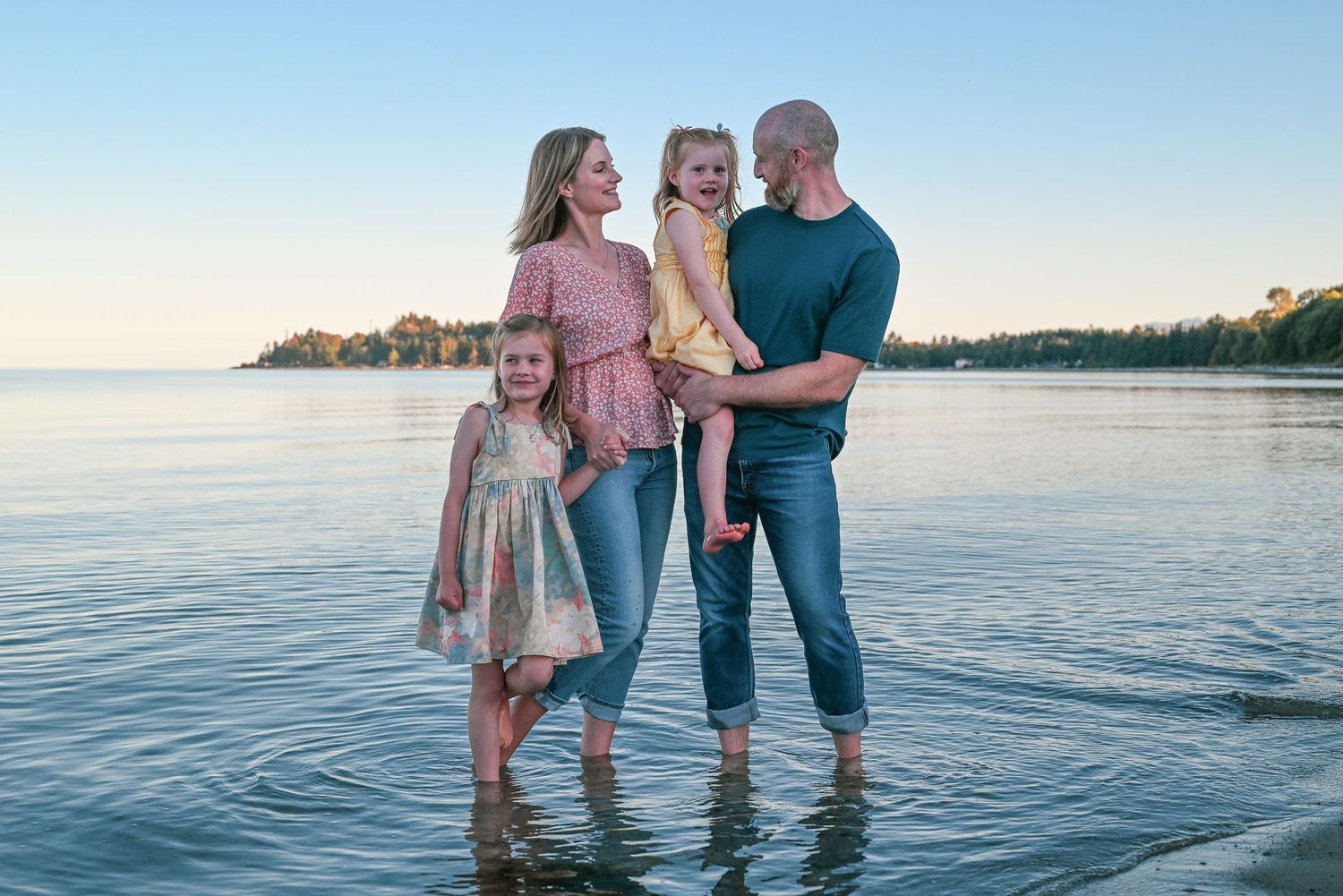 Family with two young daughters stand in the ocean.