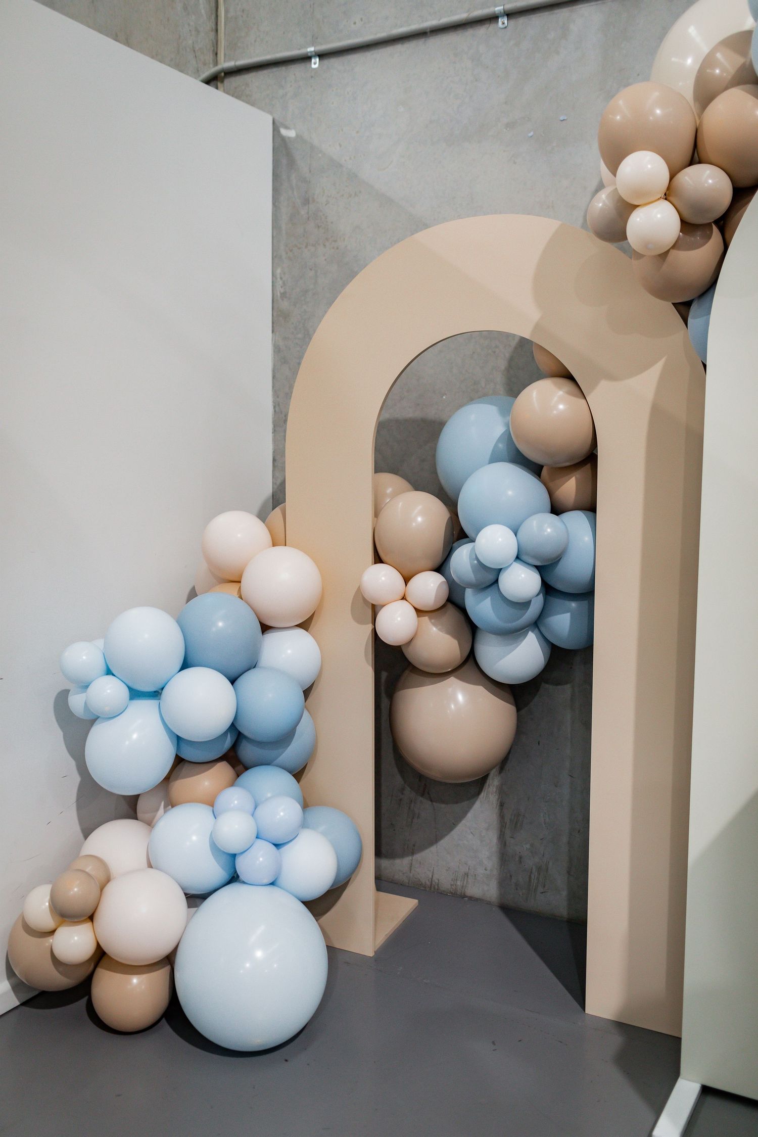 Decorative arch with blue and beige balloon installation against grey wall.