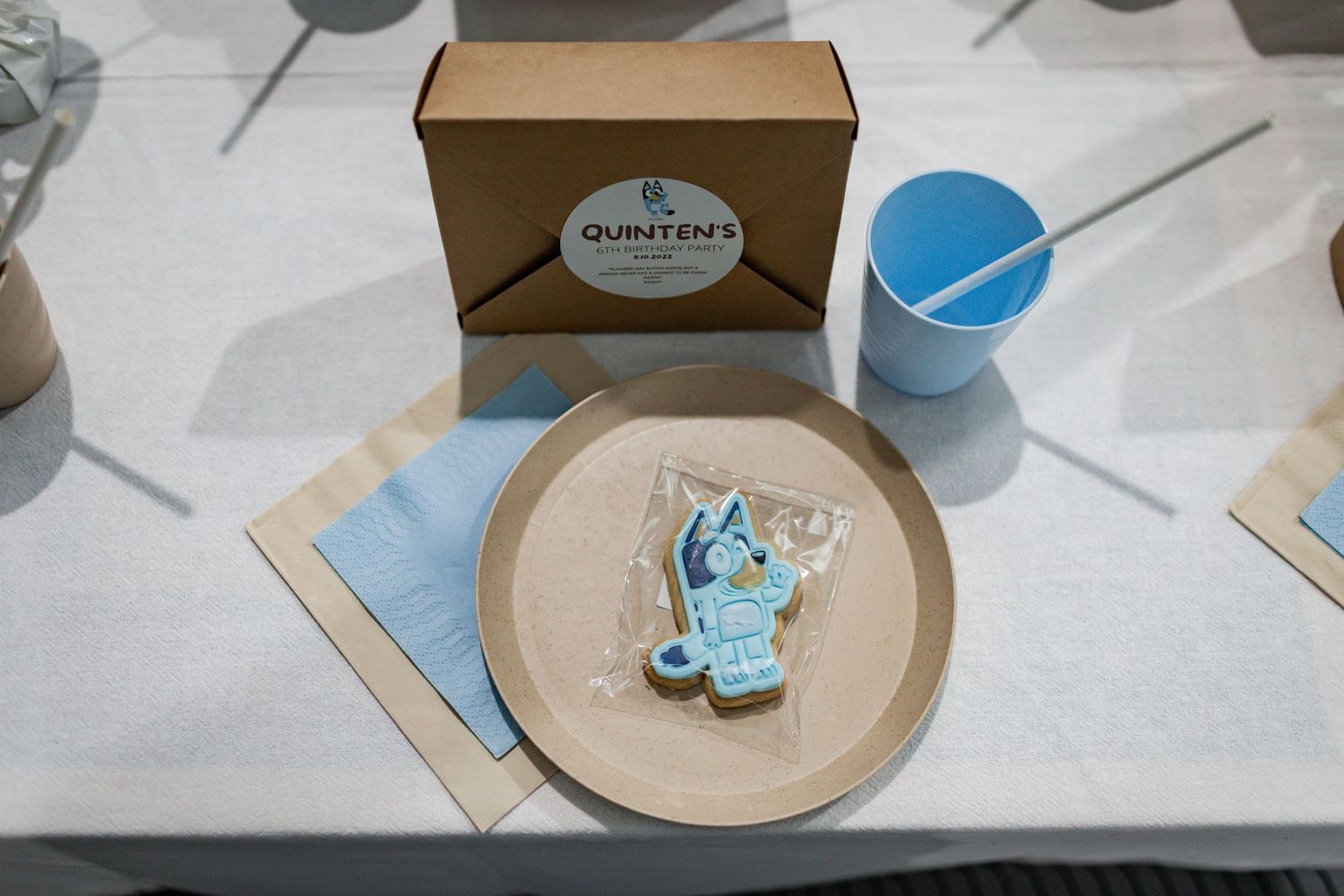 Kraft paper box with blue cookie and place setting at party table.