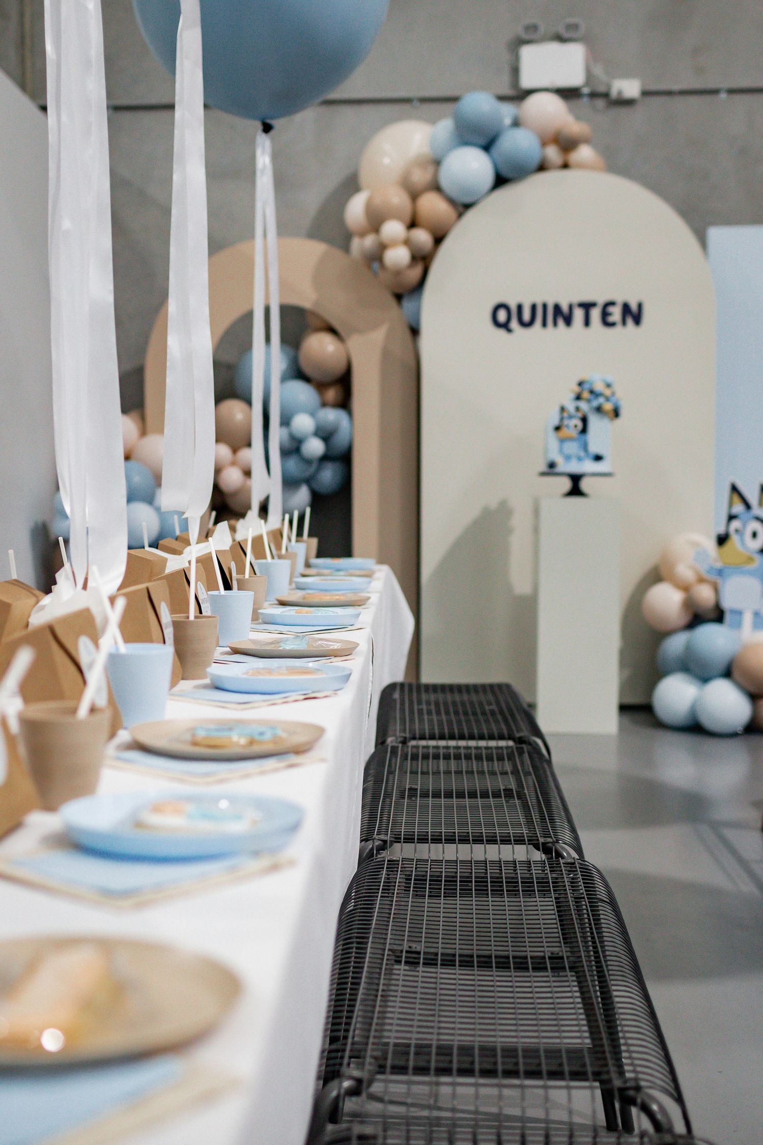 Modern party setup with blue and beige balloon garland and table settings.