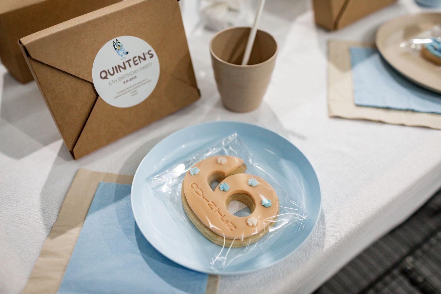 A number 5 cookie on a blue plate with kraft paper packaging labeled 'Quinten's'.