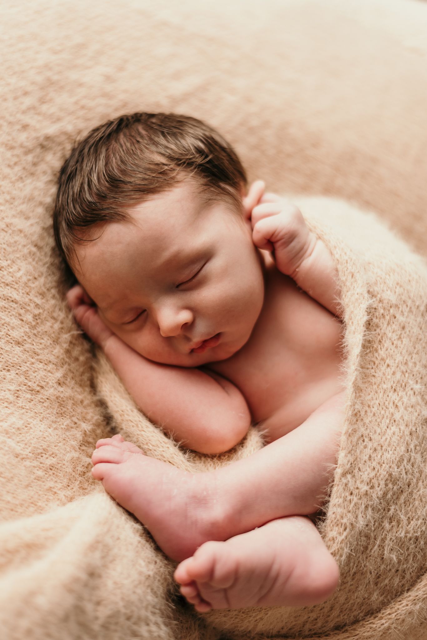 Peaceful newborn baby sleeping while wrapped in soft beige blanket.
