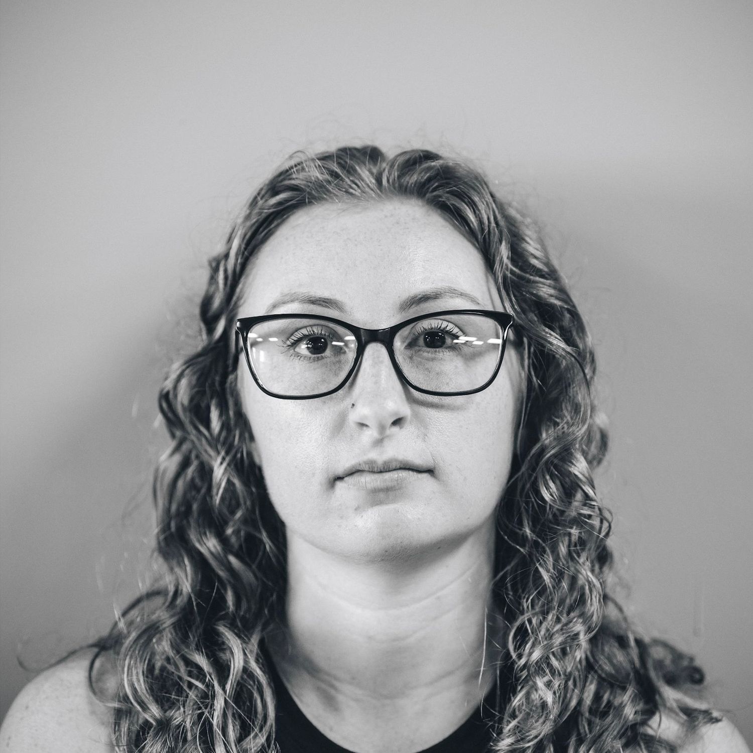 Black and white portrait of someone with glasses and curly hair looking directly at the camera.