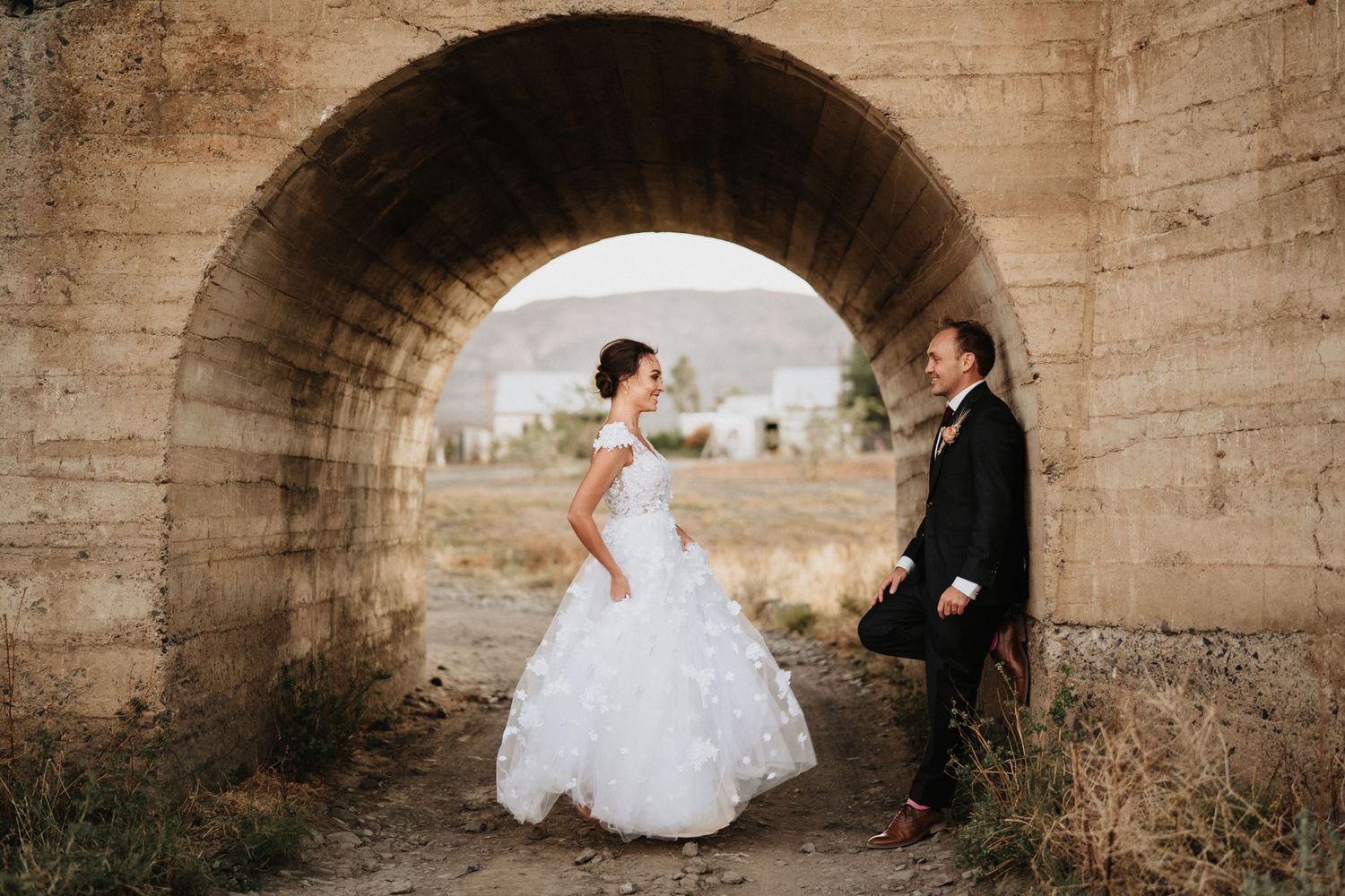 Wedding couple poses under a concrete tunnel archway in dramatic lighting.