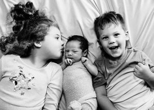 Black and white photo of two siblings lying beside their newborn baby brother or sister.