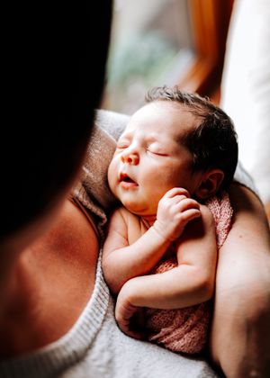 Sleeping newborn baby with dark hair resting peacefully on a parents chest in warm light.