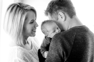 Black and white photo of smiling parents lovingly gazing at their newborn baby together.