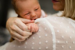 Close-up of a newborn baby resting on a mother's shoulder in a white polka dot top.