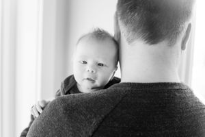 Black and white photo of a newborn baby resting on a father's shoulder, looking at the camera.