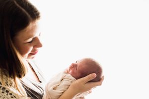 Brunette mother gazing lovingly at her sleeping newborn baby held in her hands.