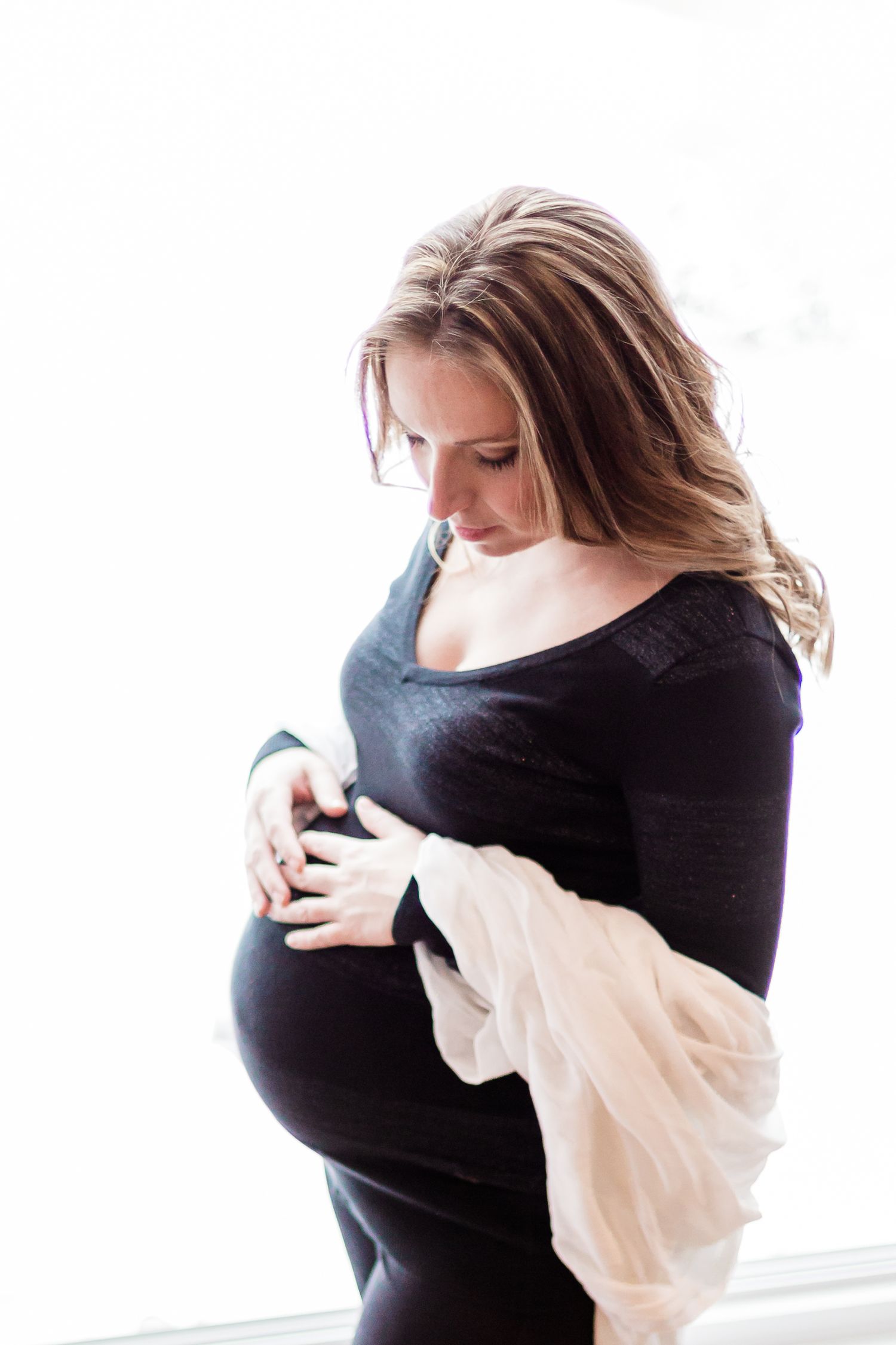 Pregnant woman in black dress cradling her baby bump with soft white background.
