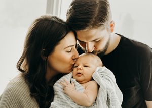 Young couple kissing their newborn baby wrapped in a gray blanket.