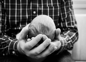 Black and white close-up of a fathers hands gently cradling a newborns head.