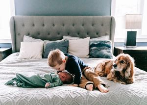 Toddler and dog resting on bed beside sleeping newborn baby.