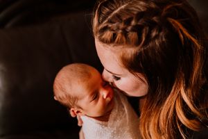 A young girl with a braided hairstyle tenderly kisses a sleeping newborn baby.