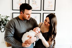 Happy couple smiling at their newborn baby held in fathers arms at home.