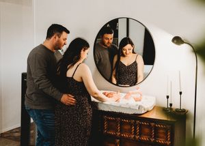 New parents admiring their newborn baby on a changing table reflected in a round mirror.