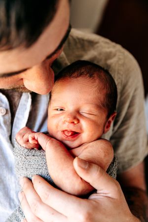 Close-up of a smiling newborn baby being held by father in warm natural light.
