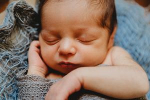 Peaceful sleeping newborn baby wrapped in a soft blue knit blanket.